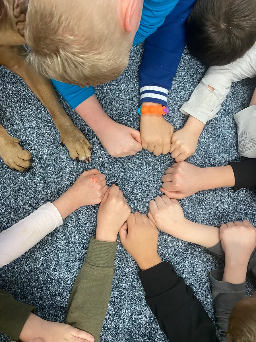 Kinderhände bilden einen Kreis um die Pfote eines Kompetenzhundes