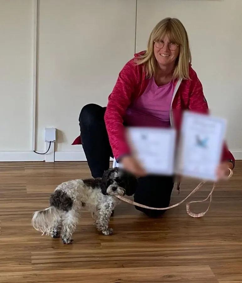 Birgit G. kniet mit Urkunde und Zertifikat neben ihrem Hund Fibi