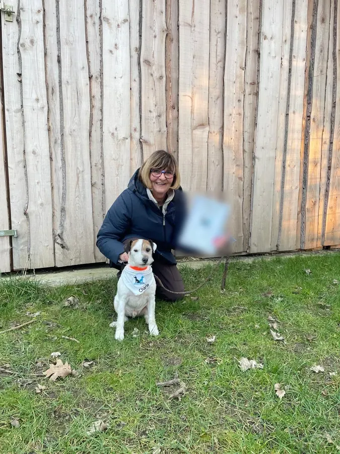 Kathrin B. hockt mit Urkunde neben ihrem Hund Charlie vor einer Holzwand