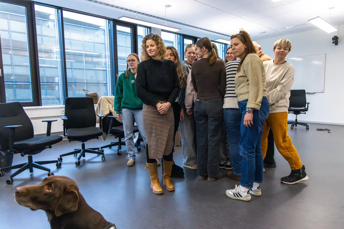 Teilnehmende einer Präsenzphase stehen mit ihren Hunden im Seminarraum